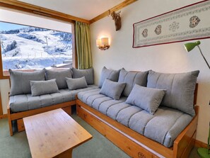 A cozy room with a sofa, a wooden table, and a view of a snowy landscape. - Charming 2-Room Apartment Méribel - 5 Pers, South Balcony, Wi-Fi (Méribel)