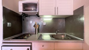 A compact kitchen with white cabinets, a stainless steel sink, a built-in oven, and a small refrigerator.