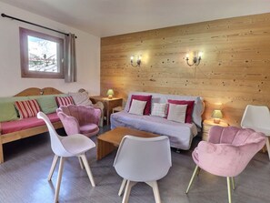 Una sala de estar acogedora con una pared de madera, un sofá, dos sillones, una mesa de centro y una ventana con cortinas.