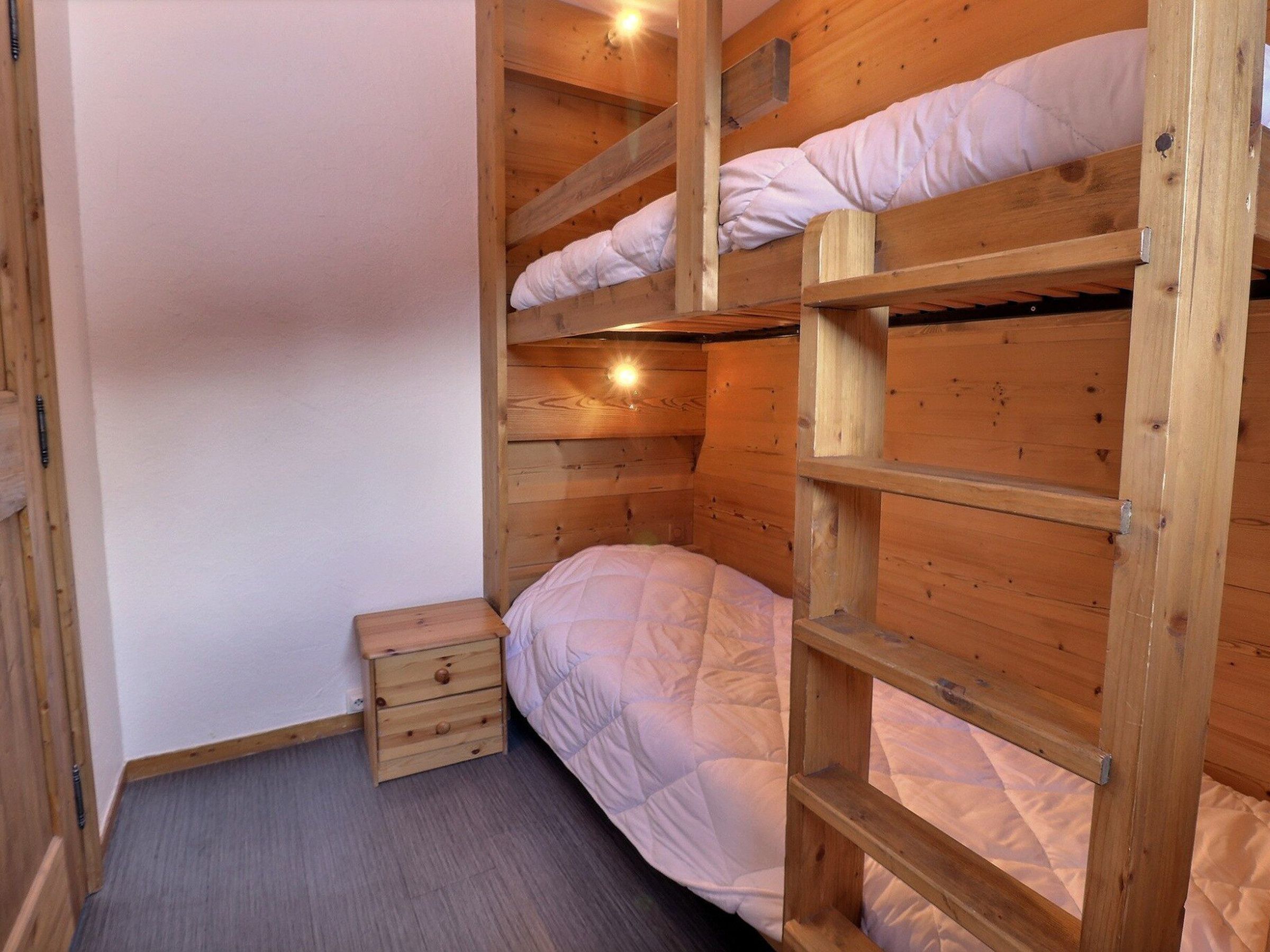 A bunk bed room with wooden walls and a small wooden nightstand.