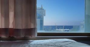 Une chambre avec vue sur un immeuble et la mer, vue à travers une fenêtre.