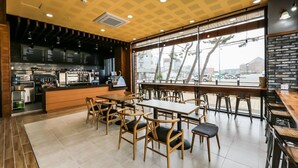 A modern cafe with wooden furniture, a bar area, and large windows offering a view of the street.
