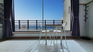 A balcony with a view of the sea, white chairs, and a table.