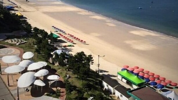 A beach with umbrellas and a building with a green roof.