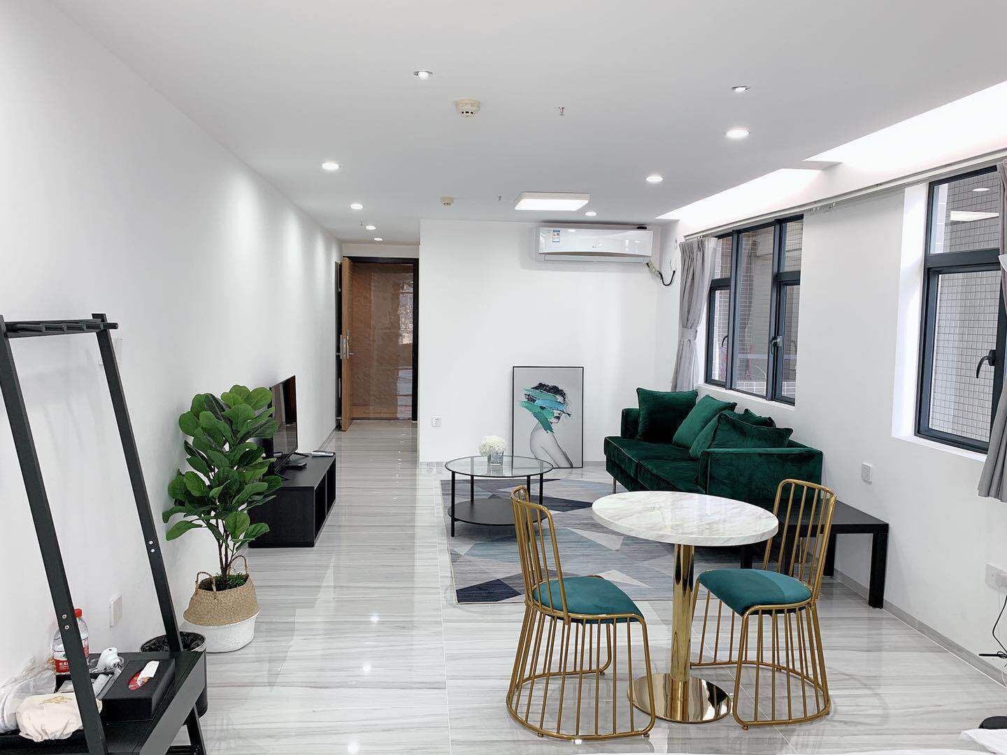 A modern, well-lit room with a round table, two chairs, a green sofa, and a large window.