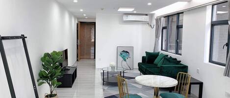 A modern, well-lit room with a round table, two chairs, a green sofa, and a large window.