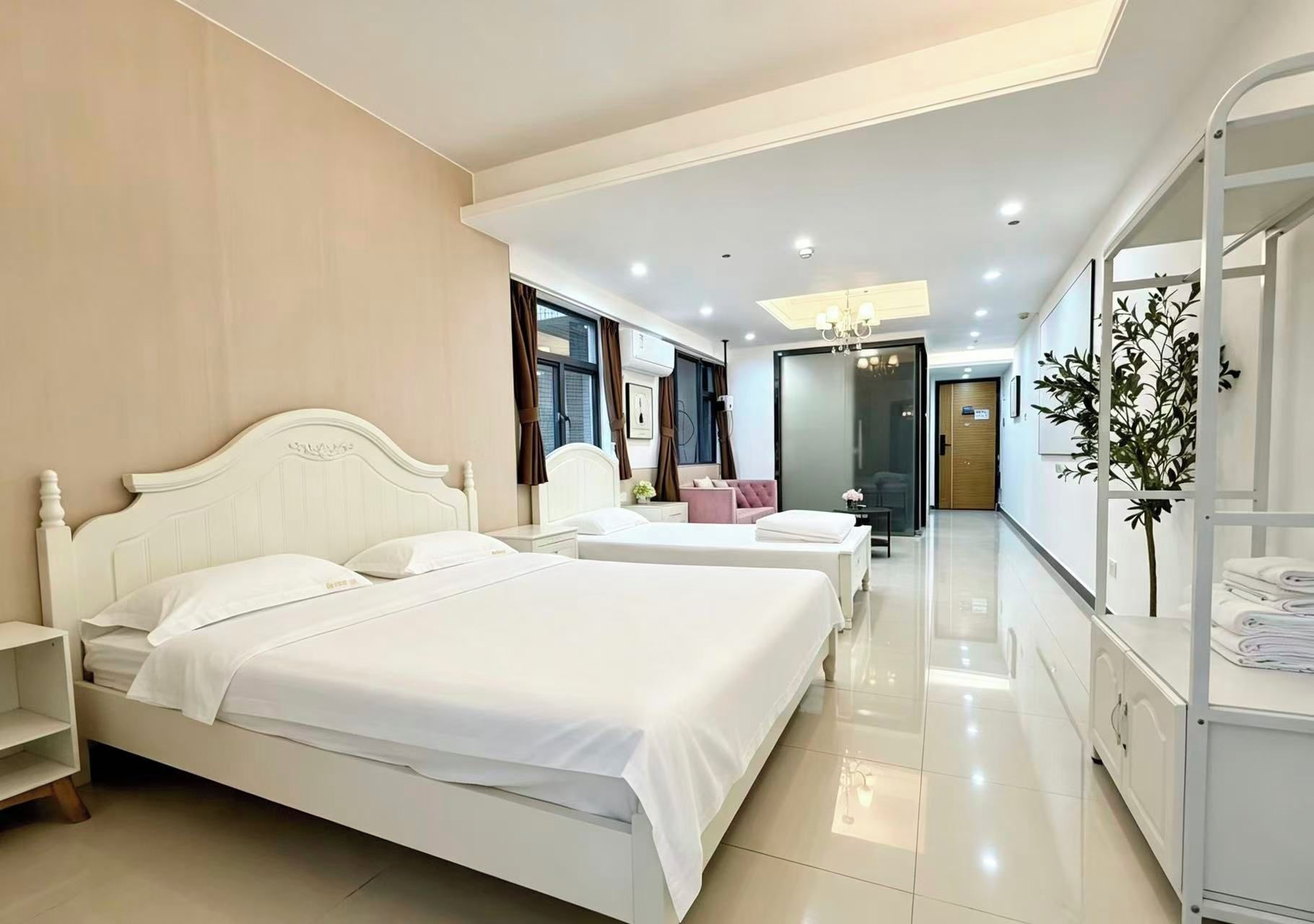 Une chambre d’hôtel avec deux lits, une armoire, un bureau et une salle de bain visible à travers une porte en verre.