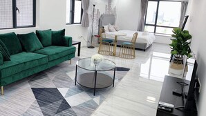 Un salon moderne avec un canapé vert, une table basse en verre et un lit orné d’une fresque représentant un paysage urbain.