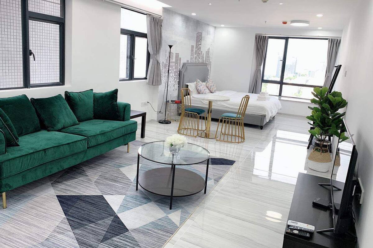 Een moderne woonkamer met een groene bank, een glazen bijzettafeltje en een bed met een stadsgezicht op de muur.