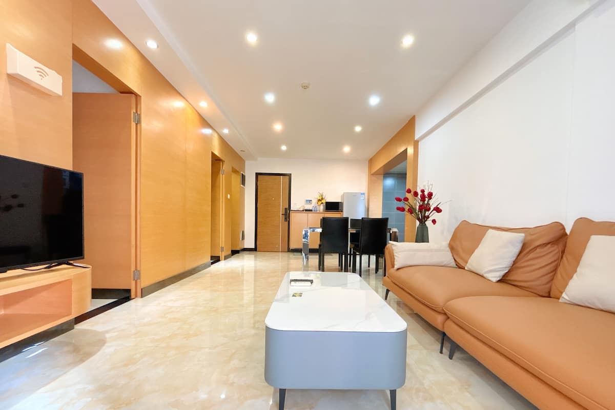 Een moderne woonkamer met een flatscreen televisie, een witte salontafel, een bank en een eethoek met stoelen en een tafel.