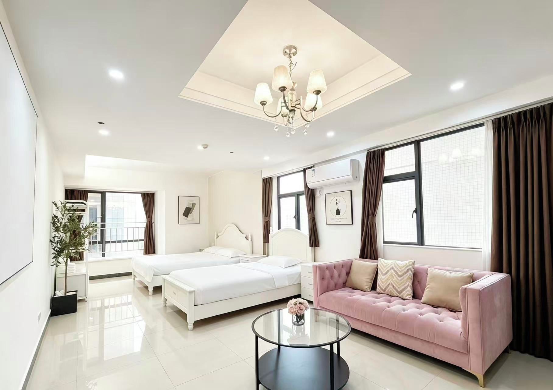 A modern hotel room with a large bed, a pink sofa, a glass coffee table, and a ceiling light fixture.