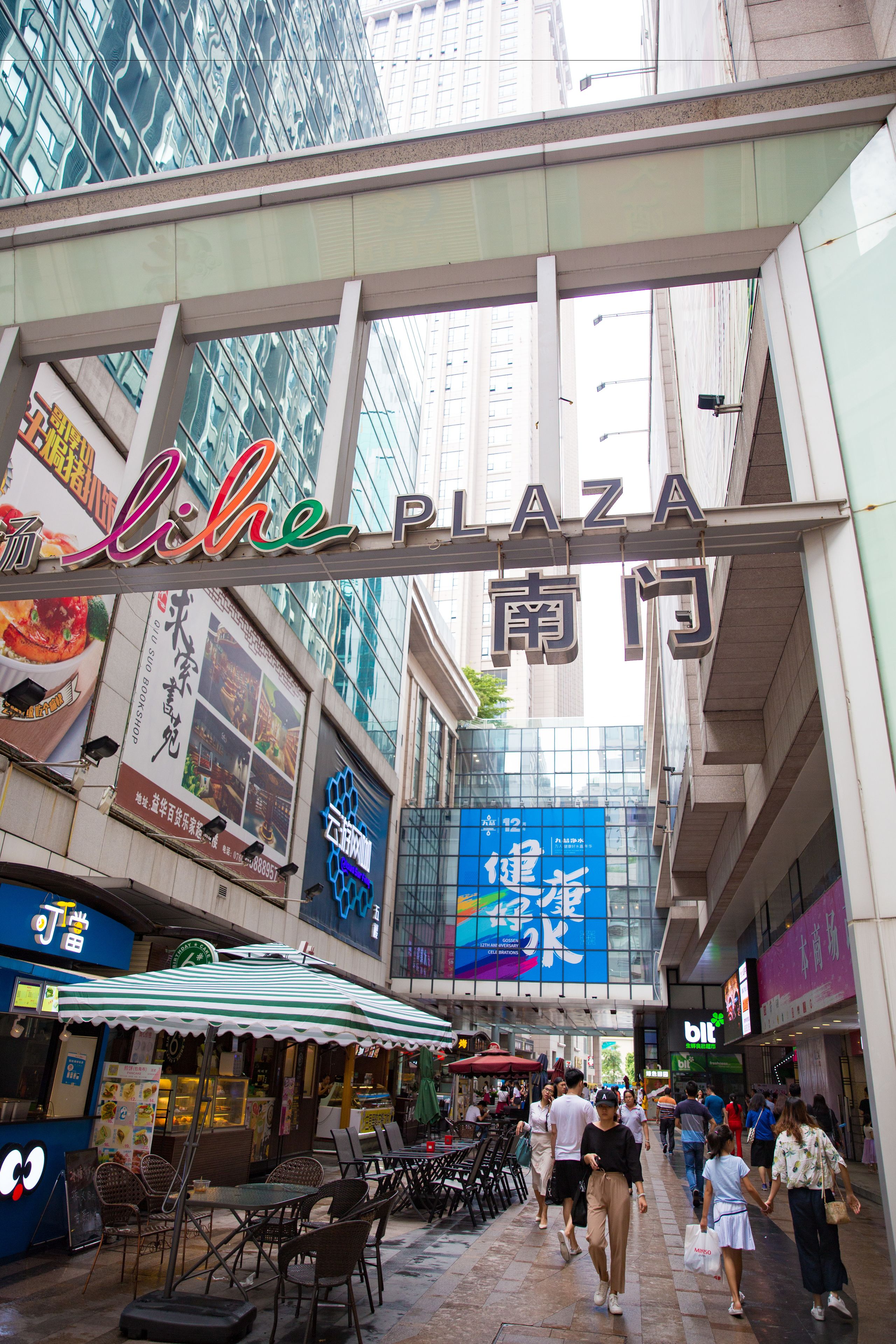 Une promenade piétonne avec des espaces de repos en plein air, une enseigne indiquant « Lihai Plaza » et diverses devantures de magasins.