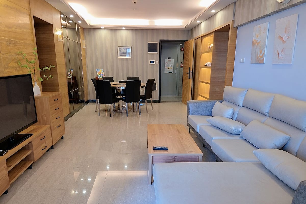 Een moderne woonkamer met een televisie, bank, salontafel, eettafel, stoelen en een tv-meubel.