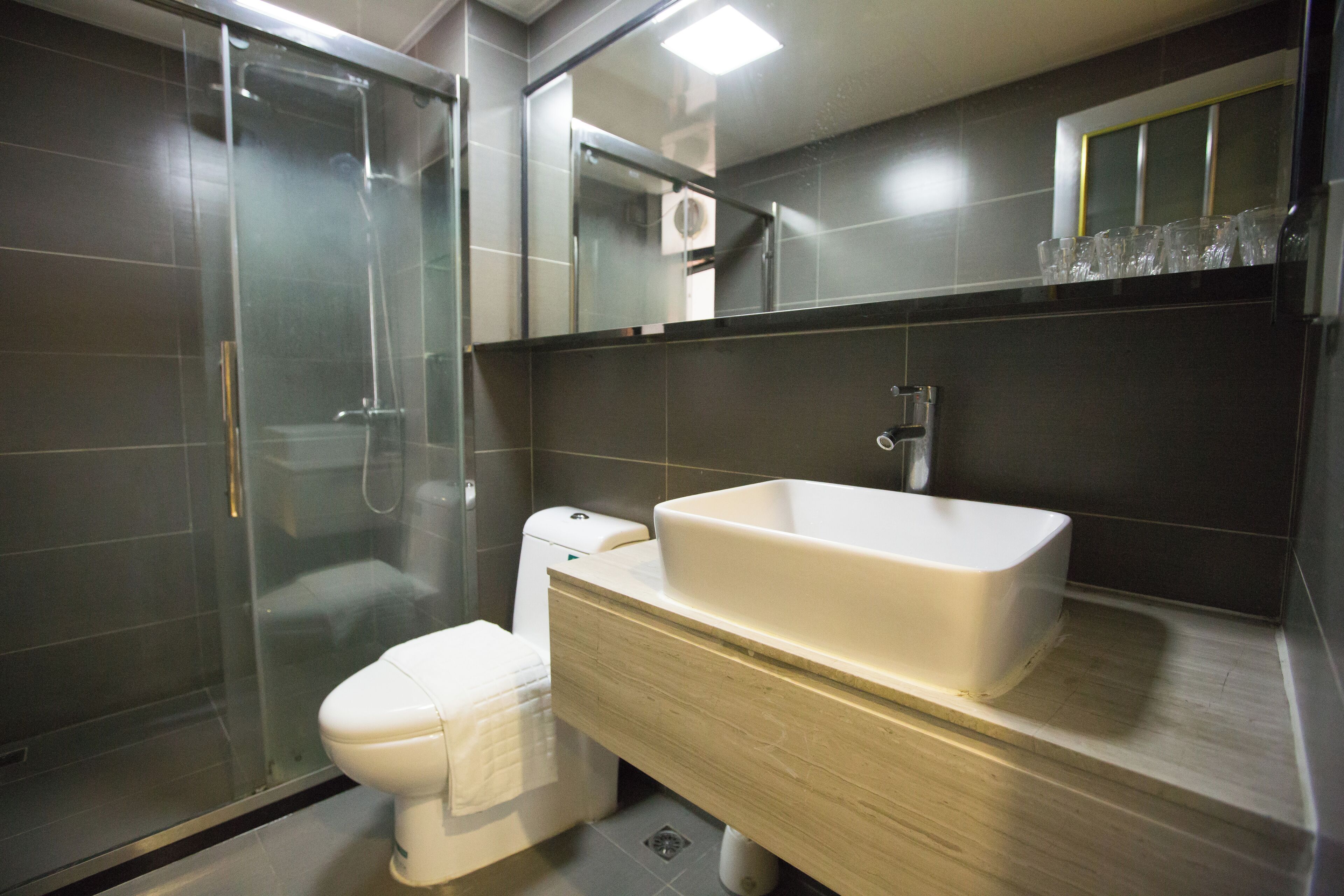 Un baño moderno con ducha de vidrio, inodoro blanco y un lavamanos grande con espejo superior.