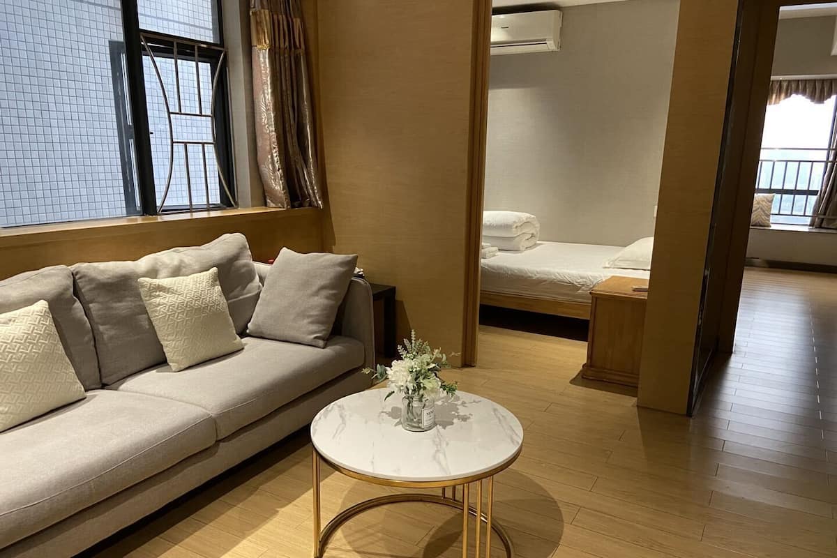 Een moderne woonkamer met een beige bank, een ronde salontafel en een bed op de achtergrond.