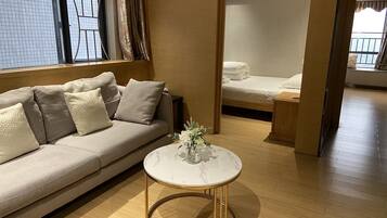A modern living room with a beige sofa, a round coffee table, and a bed in the background.