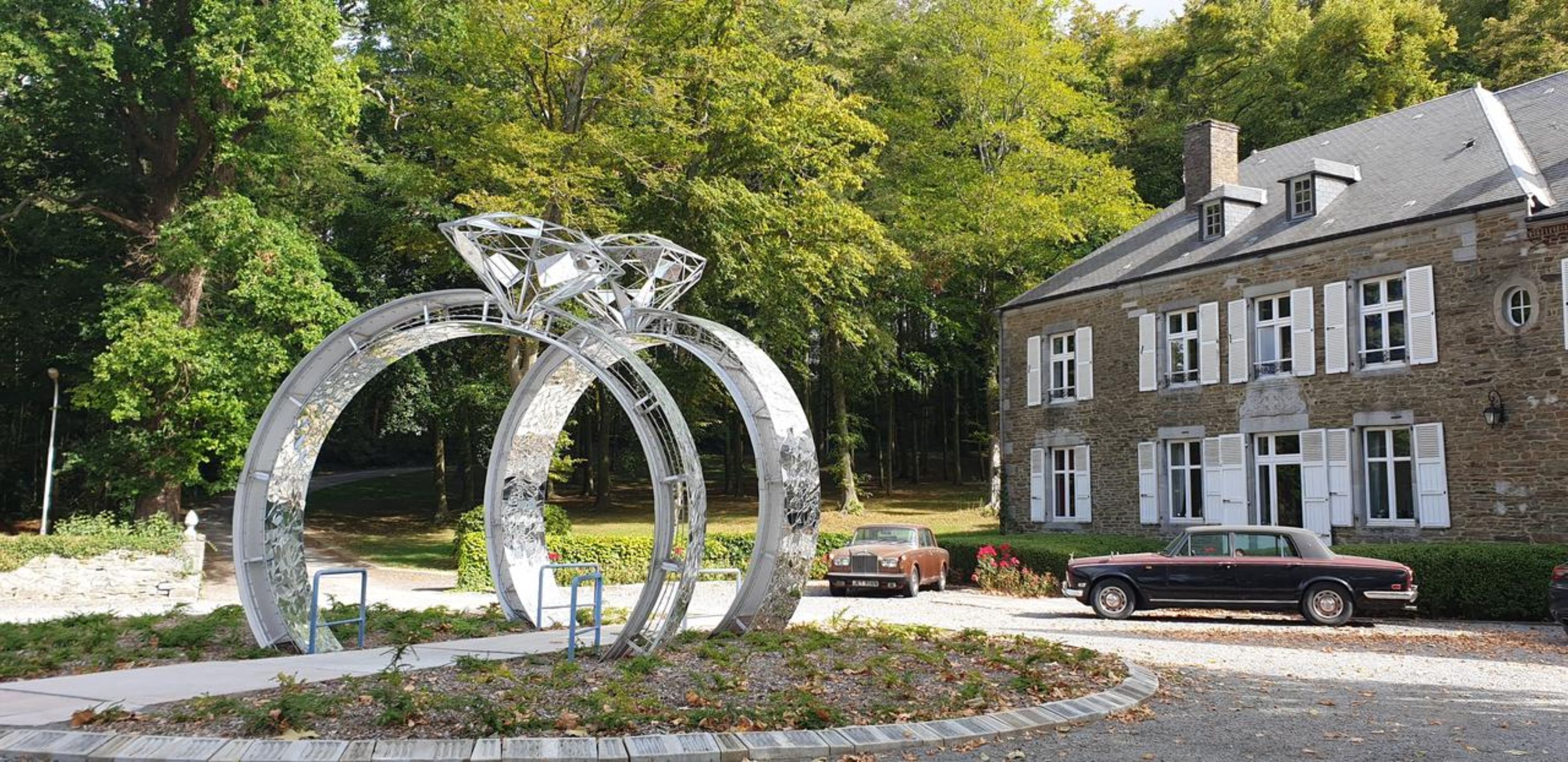 A stone building with a garden and a metal sculpture.