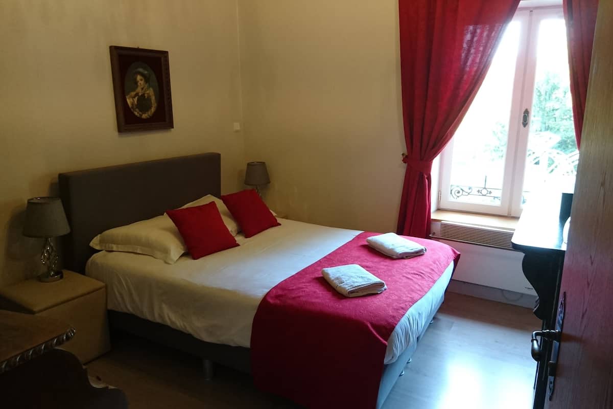 A bedroom with a bed, red curtains, a window, a lamp, and a picture on the wall.