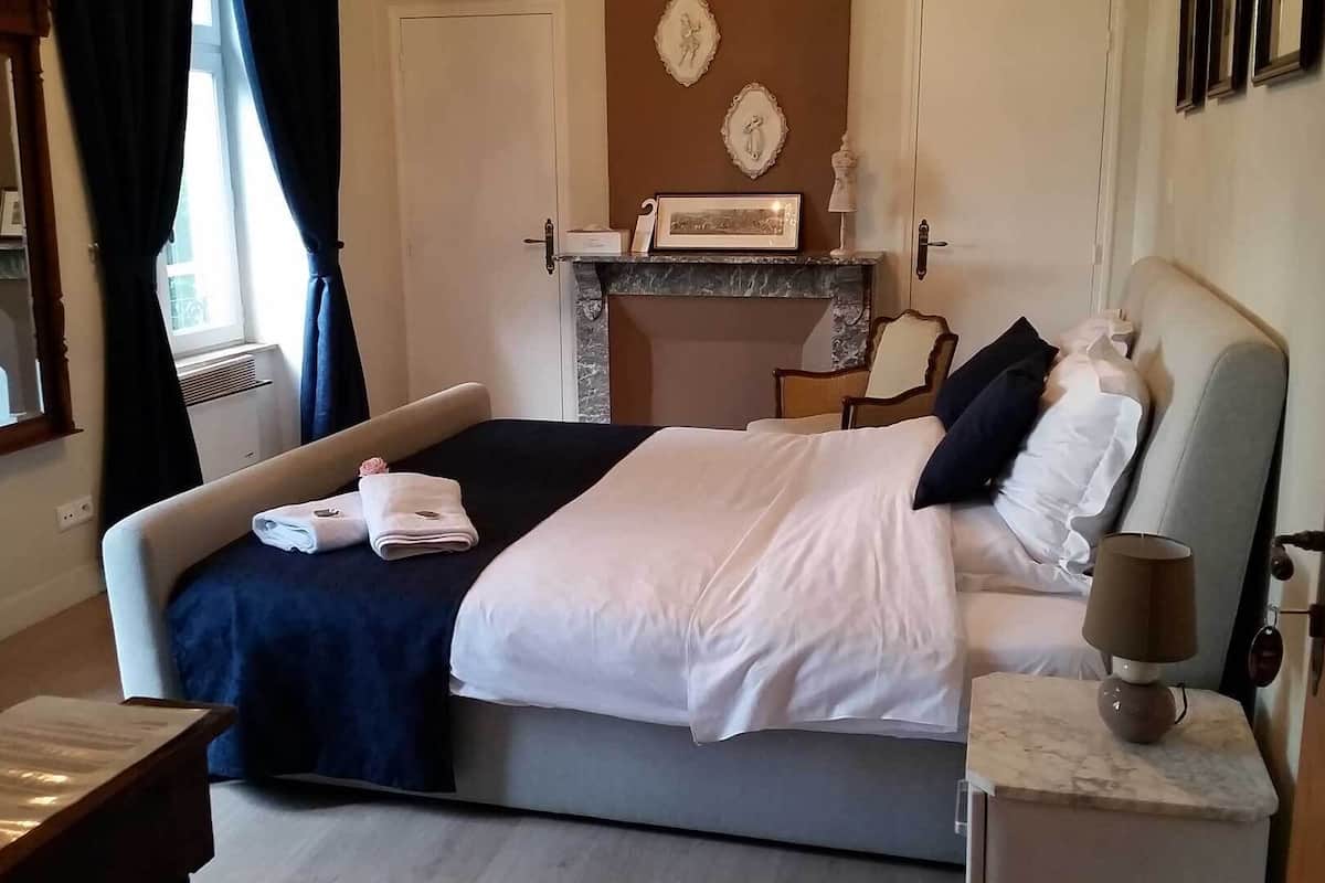A hotel room with a bed, a nightstand, a lamp, and a fireplace.