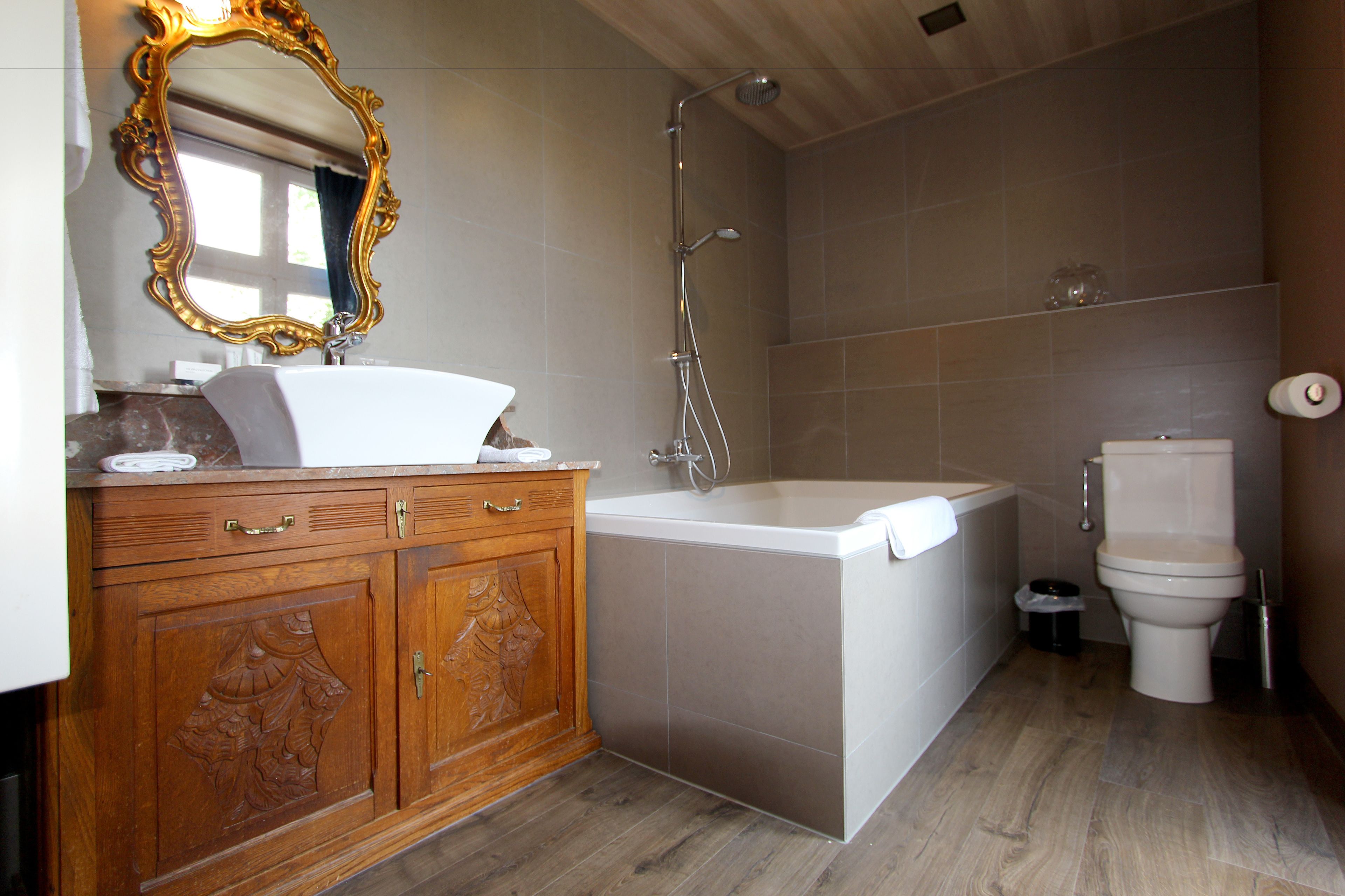 Un baño con tocador de madera, bañera blanca, ducha y retrete.