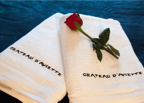 Two white towels with 'CHATEAU D'AVIETTE' embroidered on them, placed on a blue textured surface. - Château de l’Aviette (Rancennes)