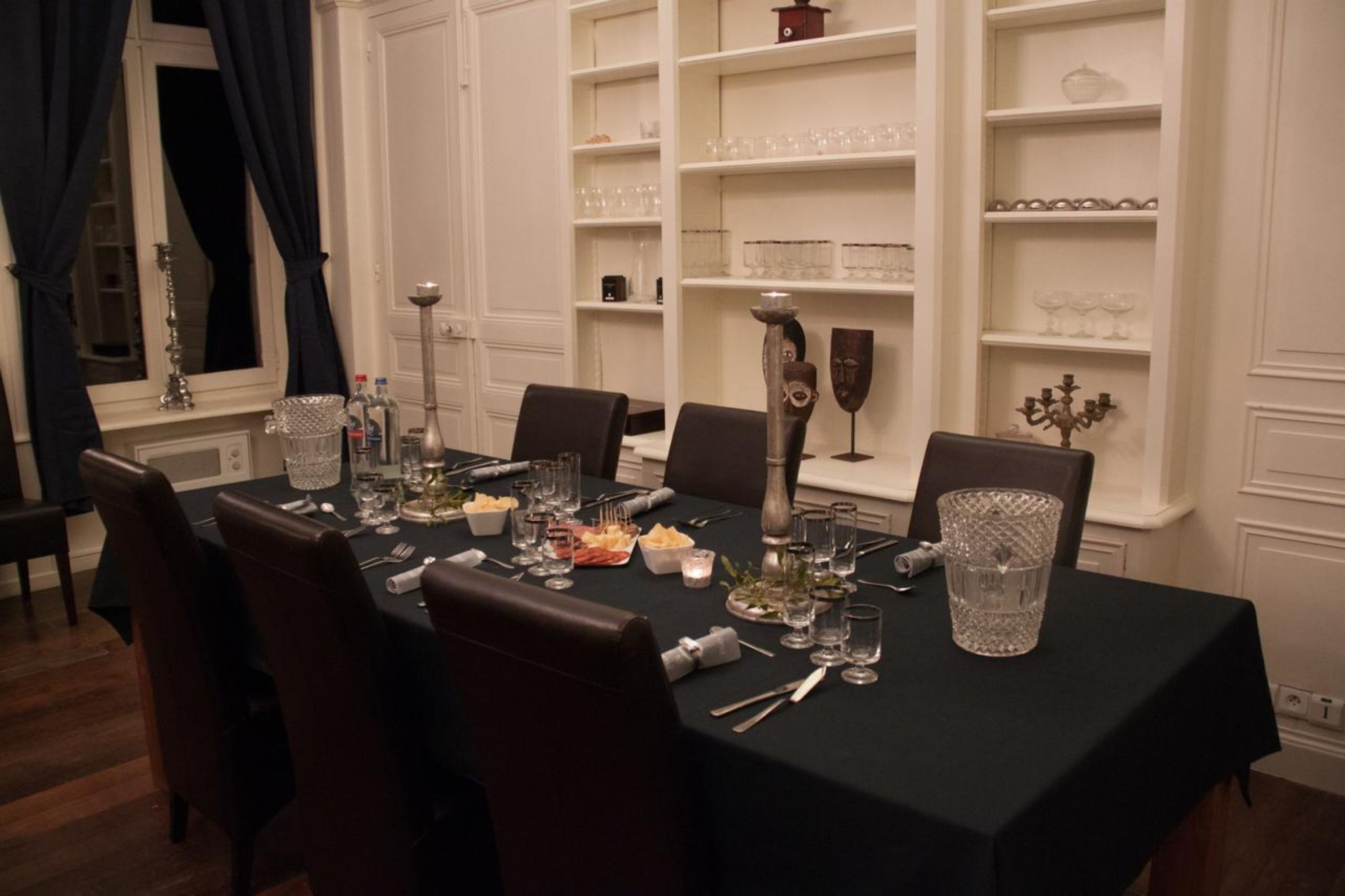 Un comedor formal con una mesa dispuesta para seis personas, rodeado de estanterías blancas con cristalería.
