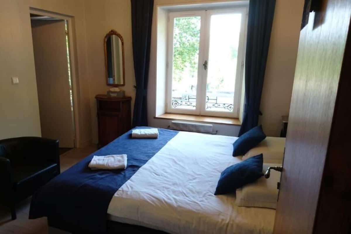 A bedroom with a bed, a chair, a window with curtains, and a door.