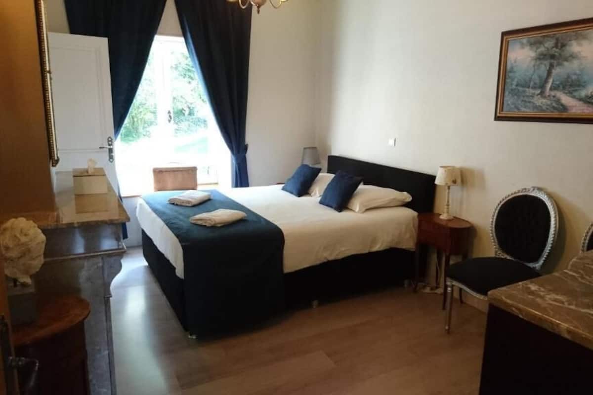 A bedroom with a bed, bedside tables, a chair, and a painting on the wall.