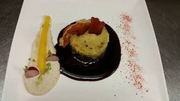 Une assiette blanche contenant un dessert composé d’un élément jaune, d’un élément rouge et d’un élément vert, le tout accompagné d’une sauce foncée.