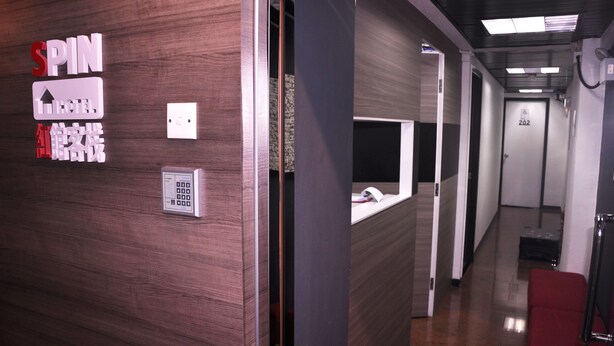 A hotel reception area with a wooden wall, a reception desk, a digital sign, and a door labeled "202".
