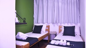 A room with two single beds, each with a pillow and a blanket. There is a small table with a chair next to one bed.