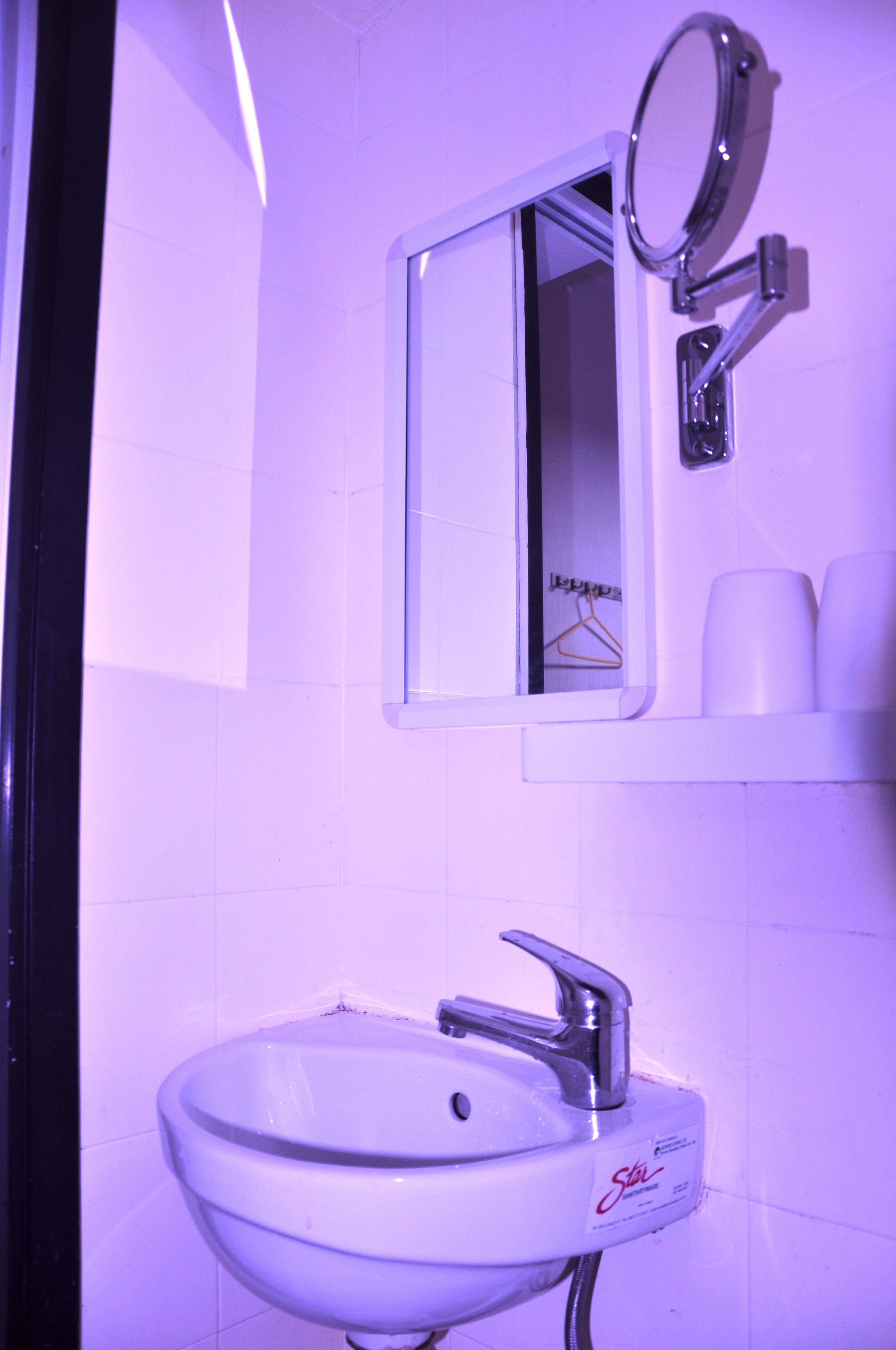 Une salle de bain avec un lavabo blanc, un miroir et un porte-vêtements suspendu.