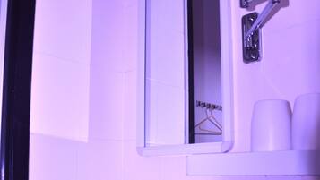 Une salle de bain avec un lavabo blanc, un miroir et un porte-vêtements suspendu.