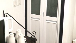 A white door with glass panels, a black metal handle, and a small black metal decoration. There are two white switches on the wall to the left of the door.