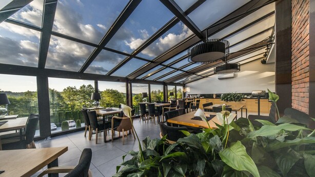 A modern restaurant with a glass ceiling, outdoor seating, and a view of the countryside.
