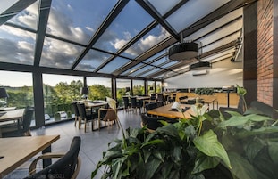 Um restaurante moderno com teto de vidro, área externa para refeições e vista para o campo.