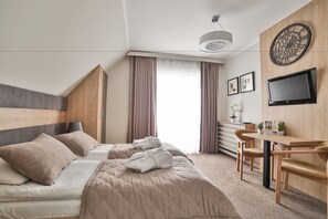 A modern hotel room with a bed, a desk, a chair, a TV, and a large clock on the wall.