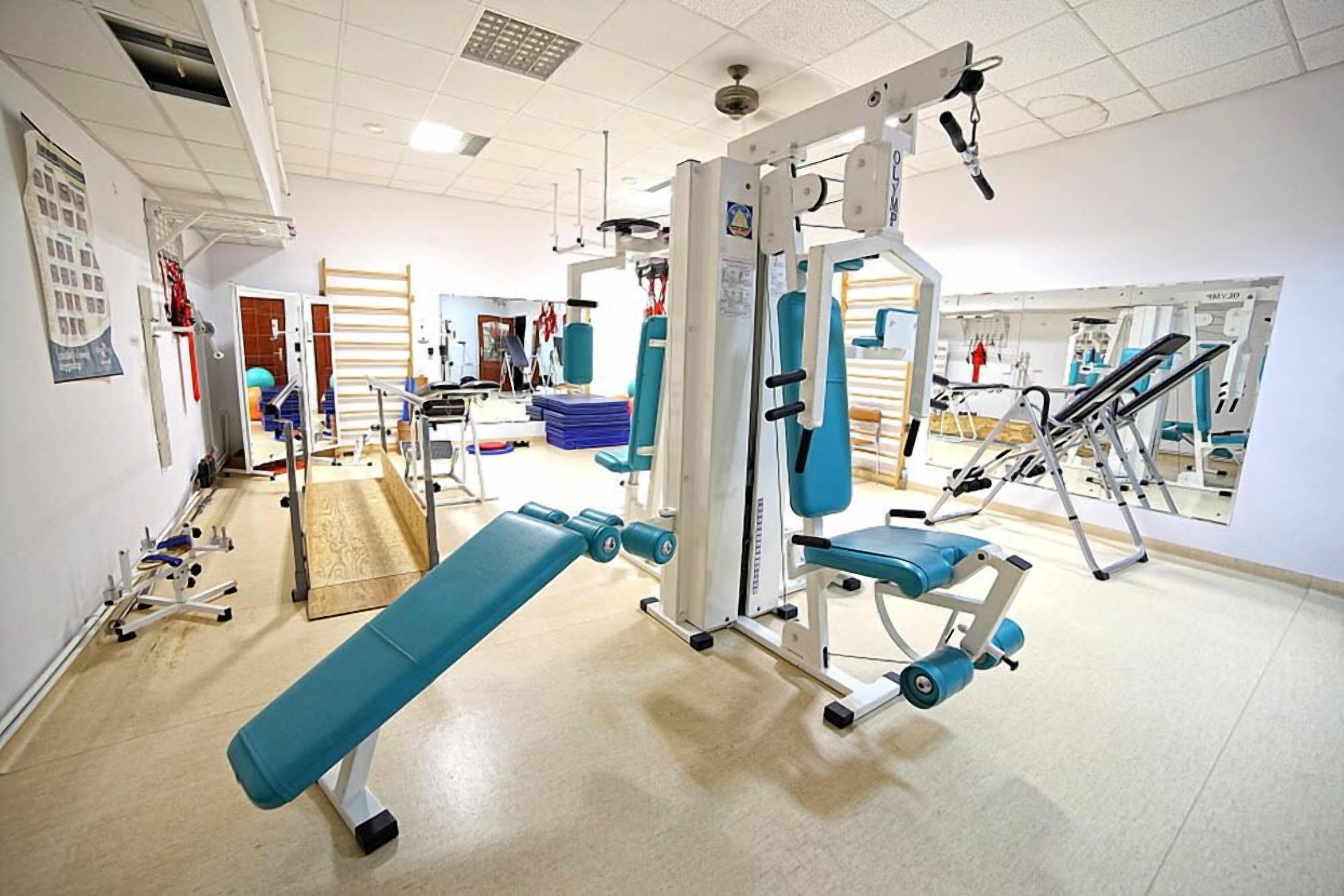 Een sportschool met trainingsapparatuur, een bank en een spiegelwand.