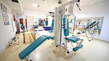Een sportschool met trainingsapparatuur, een bank en een spiegelwand.