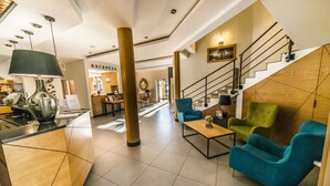 A modern lobby with a reception desk, seating area, and a staircase.