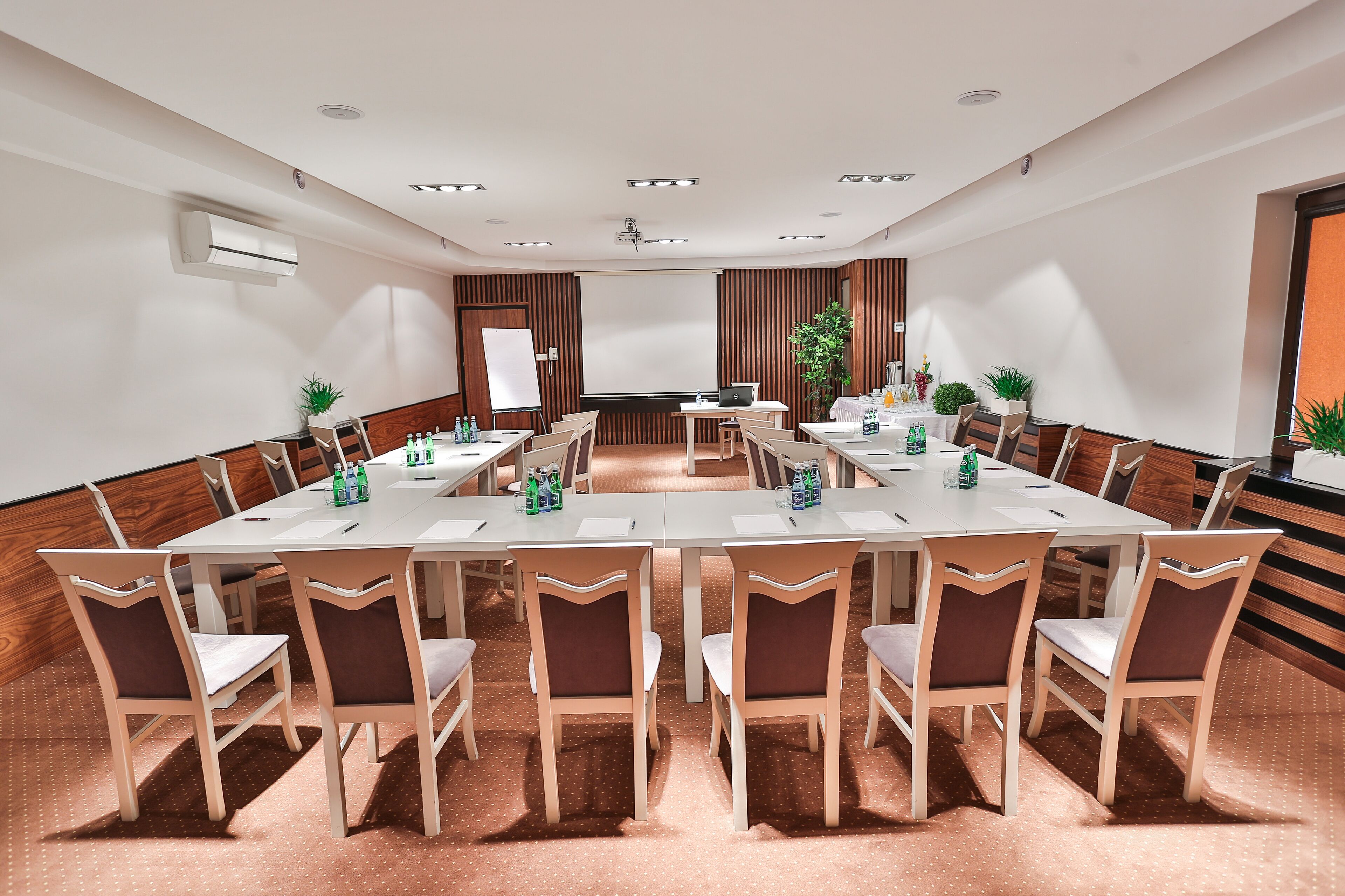 Un salón de conferencias con una larga mesa, sillas, una pantalla para proyector y una pizarra.