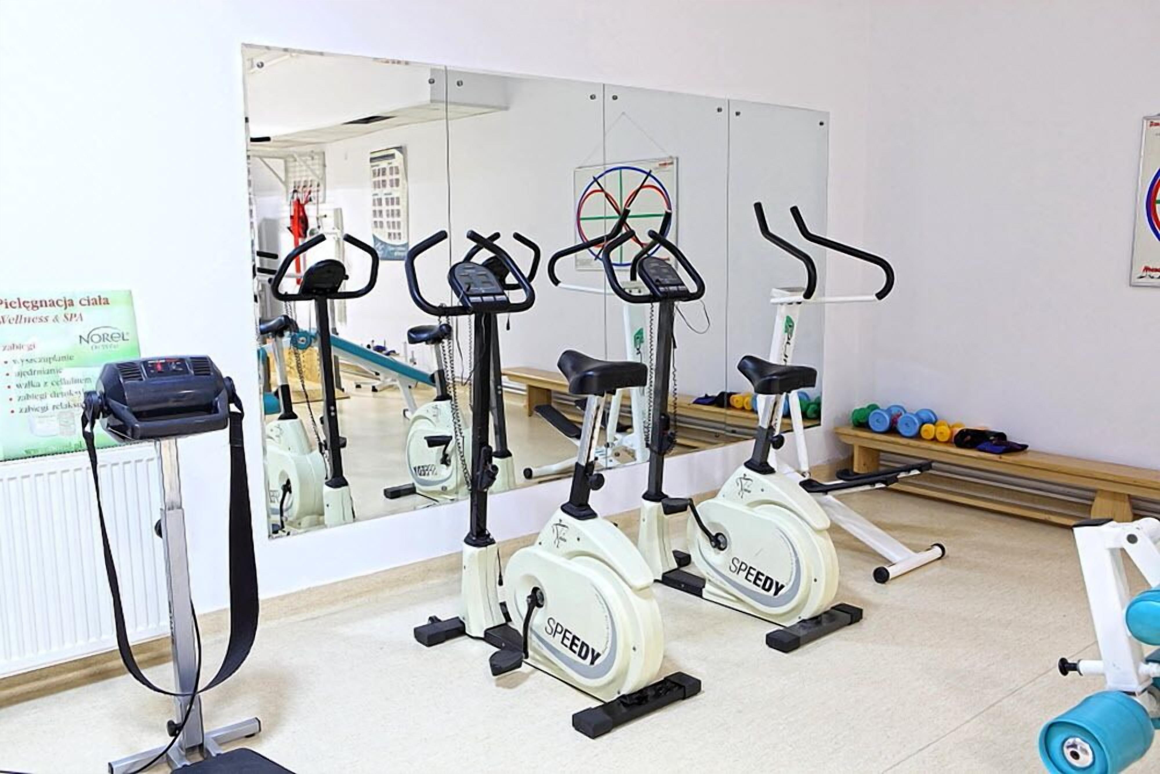 Tres bicicletas estáticas en un gimnasio, con un espejo grande que refleja el espacio.