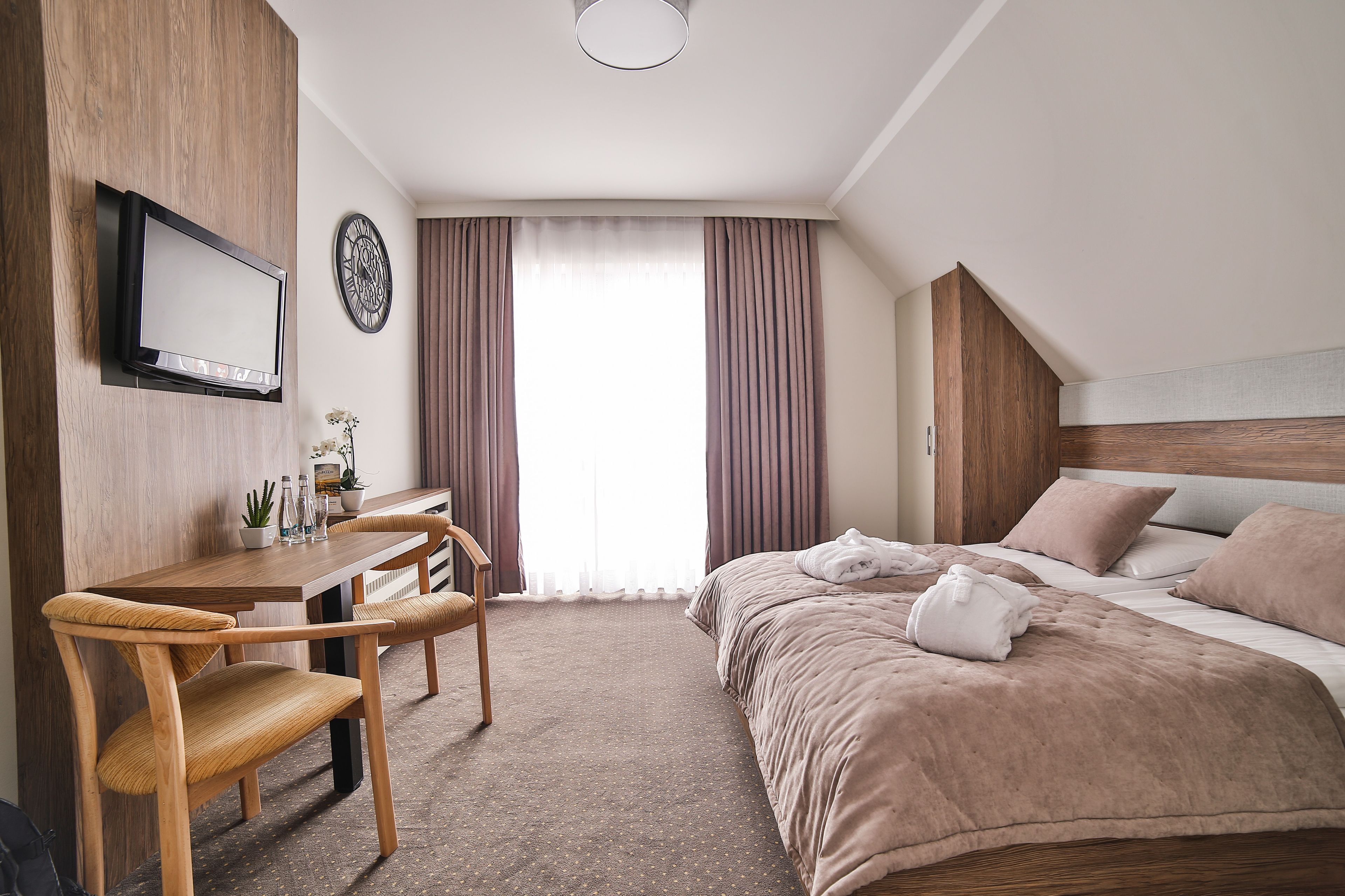 Habitación de hotel con cama, escritorio, silla, televisor y un reloj en la pared.