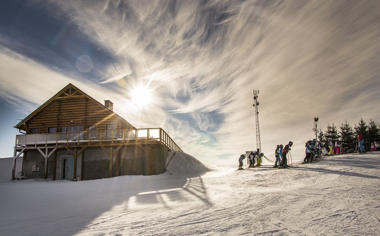 Une cabane en bois avec un balcon, un télésiège et un paysage enneigé.