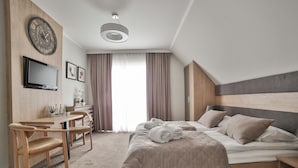 A modern hotel room with a bed, a desk, a chair, a TV, and a large window with curtains.