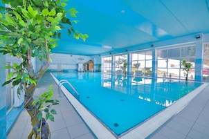 Uma piscina interna com água azul cristalina, rodeada por amplas janelas que oferecem vista para o exterior.