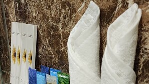 Ein Badezimmer mit Marmorwand, einem Glastablett für Toilettenartikel und zwei weißen Handtüchern.