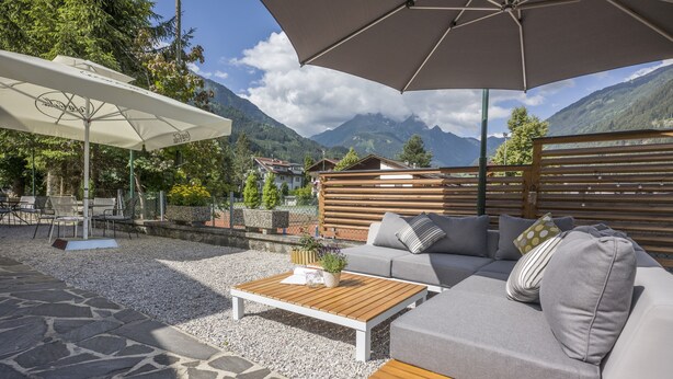 An outdoor seating area with a wooden coffee table, grey sofa, and white umbrella. - Gasthof Waldcafe (Mayrhofen)