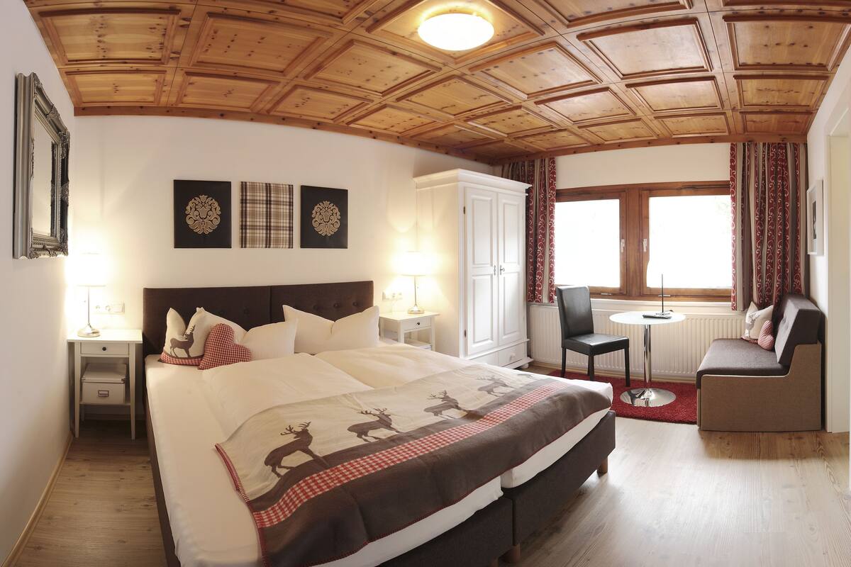 A bedroom with a large bed, a nightstand, a dresser, a chair, and a small table.