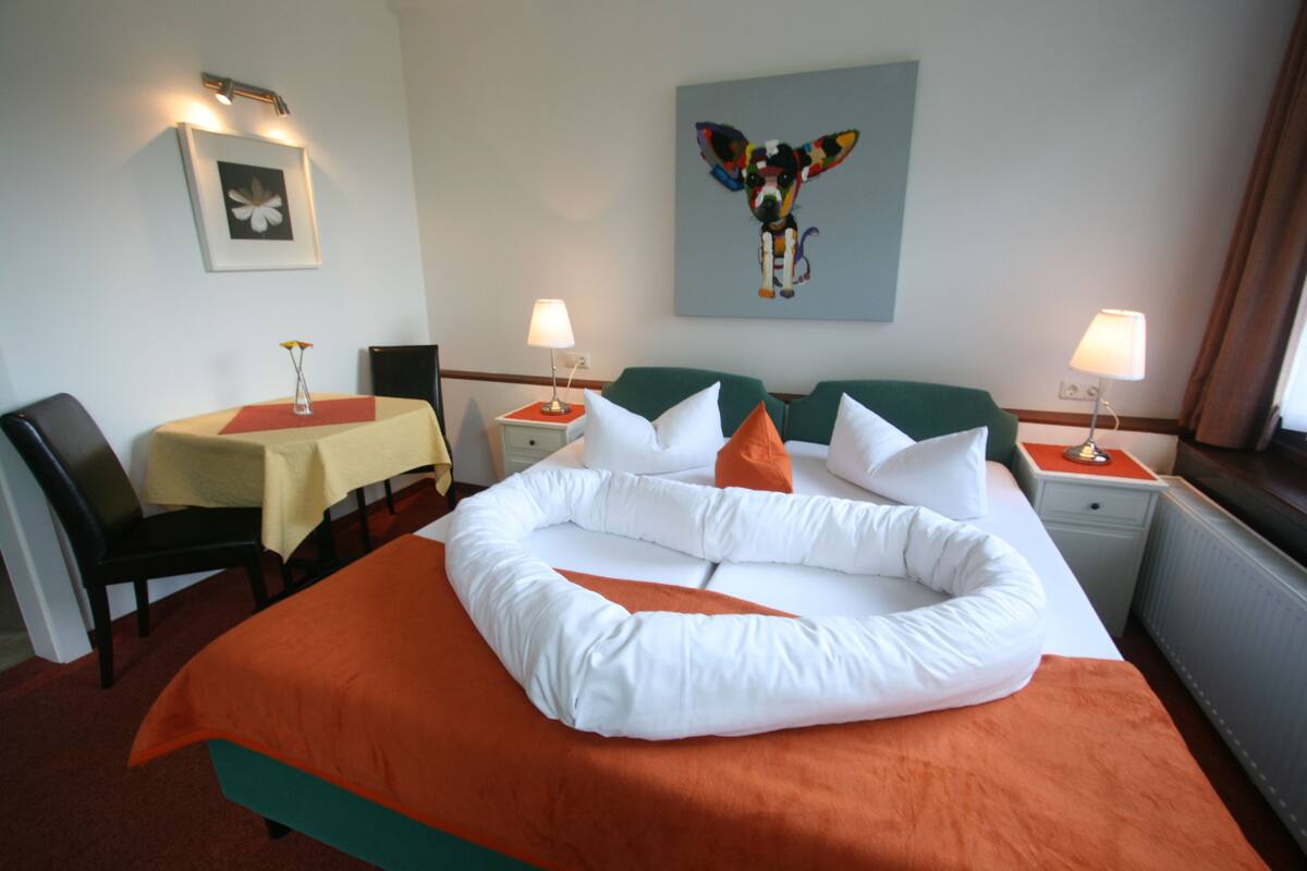 A hotel room with a large bed, two bedside tables, a chair, a small table, and a painting on the wall.